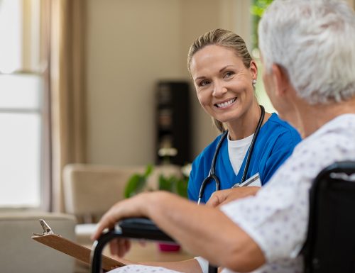 Friendly doctor examining health of patient sitting in wheelchair. Happy smiling nurse consulting disabled patient about treatment. Nurse caring about elder handicap man at home.